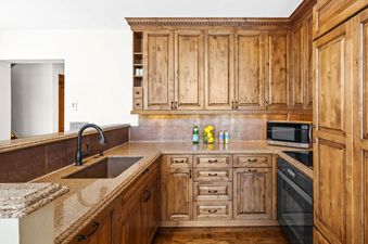 A modern kitchen with wooden cabinets and granite countertops, featuring a sink, microwave, and decorative items like lemons and sparkling water.