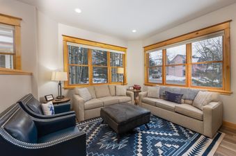 The living area at French Street Retreat features plush seating, a large rug with a geometric pattern, and views of a snow-covered landscape through multiple windows.