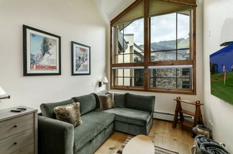 A spacious living room with a large sectional couch, a TV, and a large window with a view of a mountain landscape.