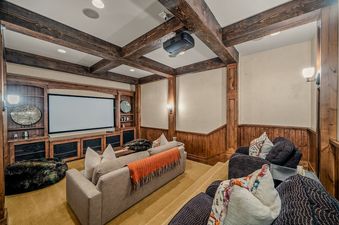 A home theater room with tiered seating, a large projection screen, and rustic wood-beamed ceilings at Mountains Edge.