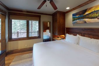 A large bed with white linens sits in a bedroom with a view of the forest out the window.