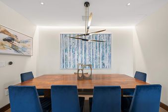 A modern dining room in One Snowmass West 301 featuring a wooden table, blue velvet chairs, and contemporary art.