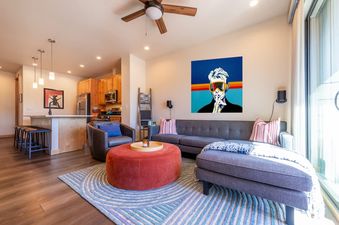 The living room at Basecamp Luxe features a large sofa, an ottoman, and a vibrant painting.