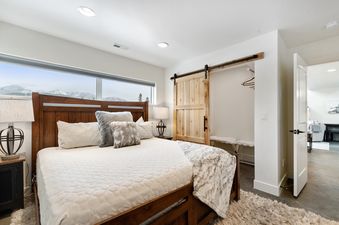 A spacious and modern master bedroom at Quarry B3, featuring a large wooden bed with white bedding, cozy pillows, a window with a mountain view, and a rustic barn door.