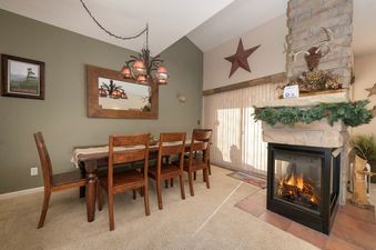 The dining area in Waterside West E206 features a wooden table and chairs, a chandelier, a wall mirror, and a cozy fireplace.