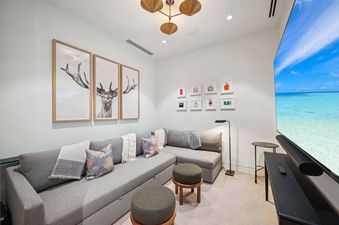 A modern media room at Founders Place 2405 featuring a large L-shaped sofa, decorative art, and a big screen TV.