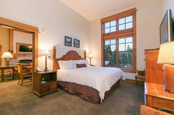 A bedroom with a king-size bed, two bedside tables with lamps, and a large window with a view of a snowy forest.