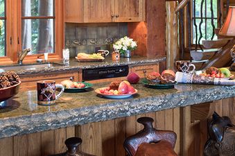 A rustic-chic kitchen with natural wood cabinets, a chiseled stone countertop, and saddle-themed barstools at the Grizzly Wulff Lodge.