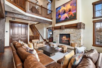 A spacious and luxurious living room at Silver Star 47, featuring a grand stone fireplace, a large leather sectional, and high ceilings with wooden beams, showcasing a rustic yet elegant design.