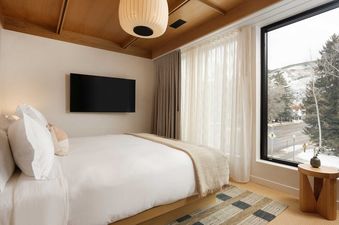 A modern bedroom in the Mollie Aspen Mollie Suite features a large bed, a wall-mounted TV, and a window with a snowy mountain view.