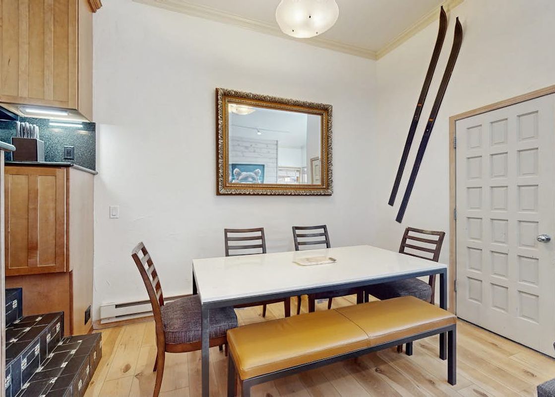 A modern dining area at Kutuk 108 with a white table, tan bench, chairs, and decorative skis on the wall.