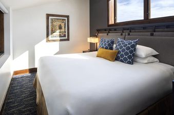 A cozy, well-lit bedroom featuring a king-size bed with white linens and decorative pillows.
