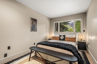 A master bedroom with a large bed, two bedside tables with lamps, and a window with a view of mountains and trees.