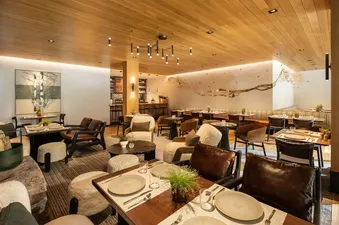 A modern and upscale restaurant interior with various seating options, including dining tables with place settings, comfortable armchairs, and a bar area.