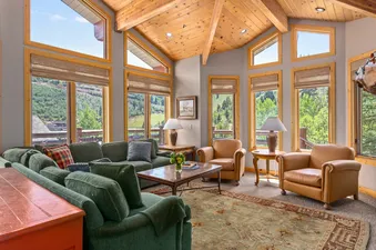 Trails End Lodge 18 features a living room with large windows, a cozy sectional sofa, a coffee table, two armchairs, and a rug on the floor.