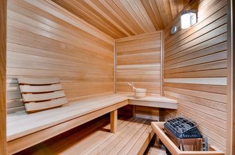 The interior of a sauna at Alders Chalet, featuring light-toned wooden walls, benches, and a traditional sauna heater with a bucket and ladle.