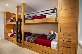 A cozy bunk room at Roaring Fork Chalet featuring custom wooden bunk beds with red bedding, plaid blankets, and integrated storage with black handles.