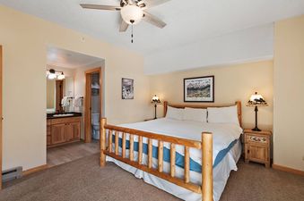 A bedroom with a king-sized bed, wood-framed windows, and a bedside table.