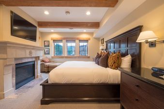 A cozy bedroom with a large bed, fireplace, and flat-screen TV.