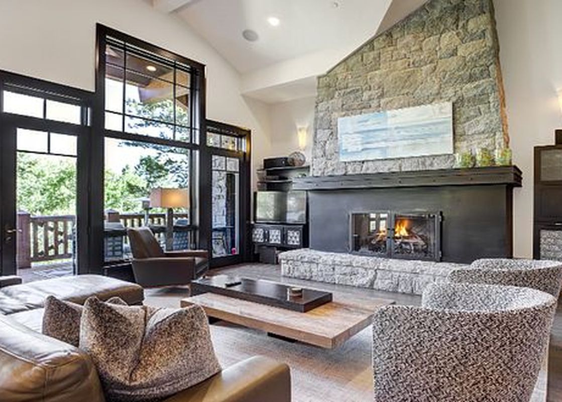 The living room of the Hummingbird Platinum 3 BR Plus Loft showcases a stone fireplace, large windows with outdoor views, and comfortable seating.