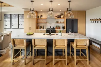 A modern kitchen and dining area in The Sylvan Lodge One Bedroom Suite featuring a large island with bar stools, light wood cabinetry, and a dining table with art on the wall.