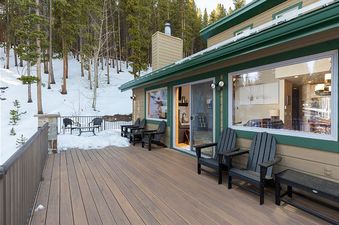 A large, spacious deck with outdoor seating, covered in a light layer of snow and surrounded by snow-covered trees, extends from 8 Crown Drive.