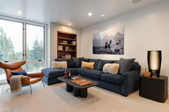 A modern lounge at West Evergreen featuring a navy blue sectional sofa and a brown leather armchair near a large window.