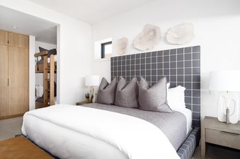 A luxurious bedroom in Moonlight Basin 8C Speedwell, featuring a large, plush bed with white linens and a cozy grey headboard, a wooden nightstand with a lamp, and a window with a view of the surrounding area.