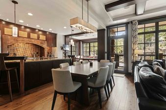 An expansive open concept living space in Flagstaff 208 featuring a dark wood kitchen, a dining area with a large table and upholstered chairs, and a living room with a leather sofa, all under high ceilings with modern lighting and offering exterior views