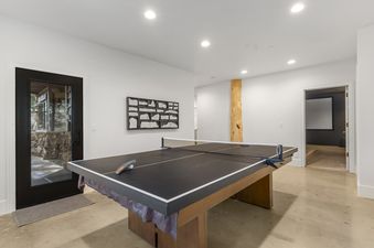 A modern games room featuring a black ping-pong table, rustic wooden art, and a glimpse of a home cinema through an open doorway.