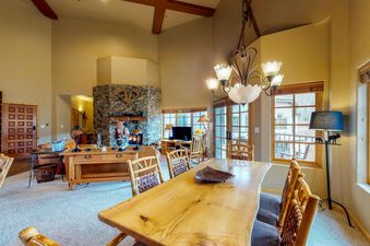 A dining table and chairs are in the foreground, with a living room and stone fireplace in the background.