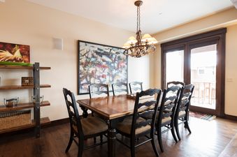 A formal dining room with a large wooden table, eight chairs, a chandelier, and abstract artwork.