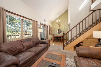 A spacious living area with a large brown leather sofa, a wooden coffee table, and a dining area visible in the background, featuring a dining table and chairs with light green accent wall.