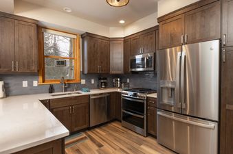 A modern kitchen with wood cabinets, stainless steel appliances, and a window overlooking a snowy landscape.