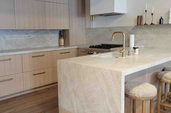 A modern kitchen at 1175 B Casolar Del Norte features light wood cabinets, marble countertops, a brass faucet, and stylish bar stools.