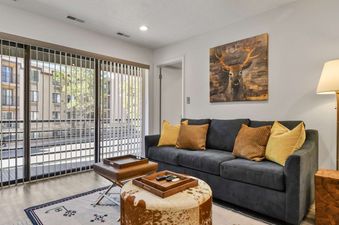 A living room with a gray couch, two pillows, a wooden coffee table, and a large window with an exterior view.
