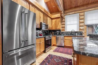 A modern kitchen in Obsidian Jackson Hole, featuring stainless steel appliances, light wood cabinets, and dark marble countertops.