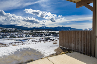 The image shows a vast mountain landscape covered in snow, with a small town nestled in the valley below, under a bright blue sky with scattered clouds.