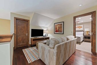 A cozy living area at Ascent 405 with a patterned sofa, a large TV, and a colorful striped rug, next to a bedroom entrance.
