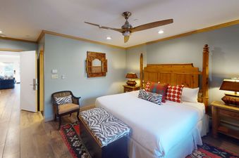 A bedroom with a white bed and a wood headboard, a zebra print throw blanket, and a wood side table with a lamp.