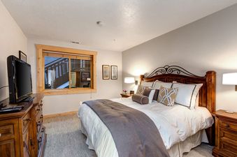 A spacious bedroom at Black Bear 152 with a large bed, nightstands, and a window looking out to a mountain view.