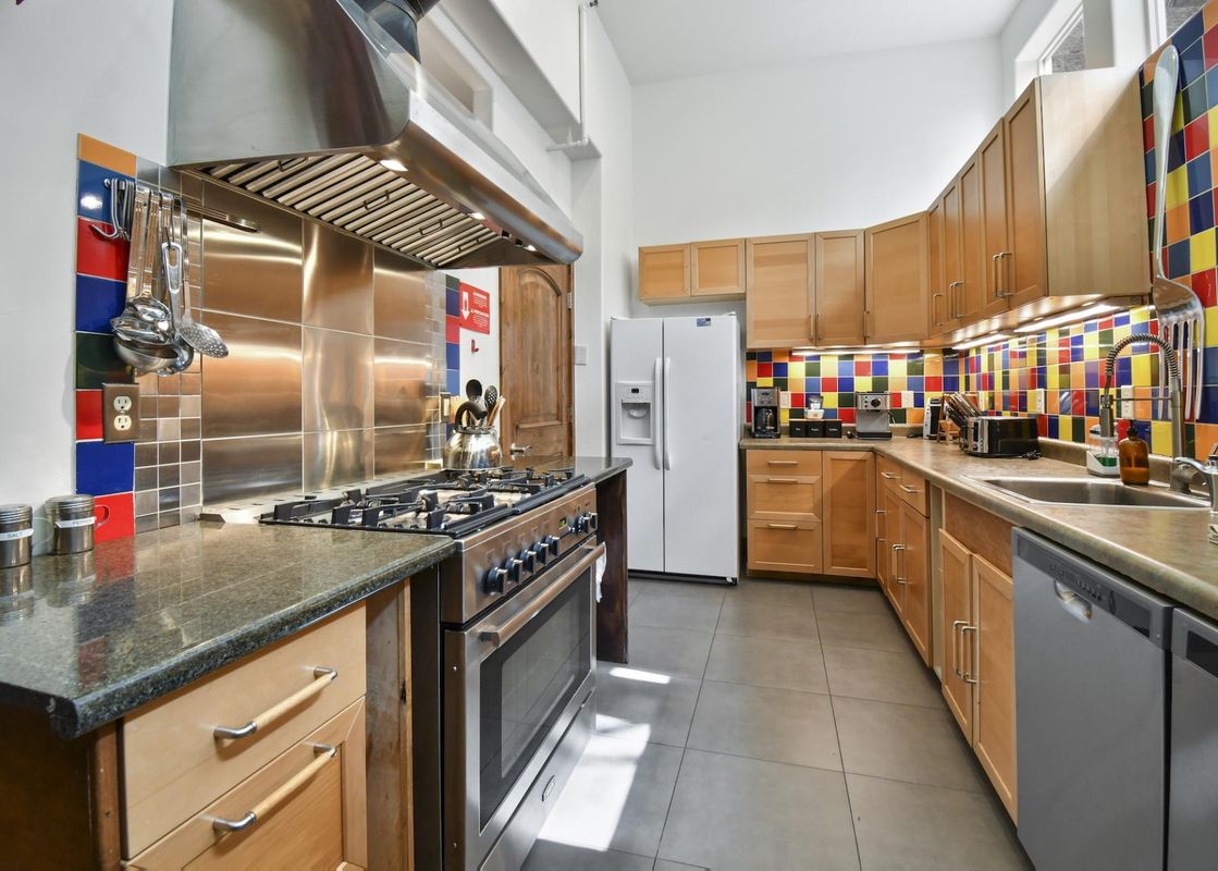 A modern kitchen in The Pearl of Park City featuring light wooden cabinets, granite countertops, stainless steel appliances, and a colorful tiled backsplash.