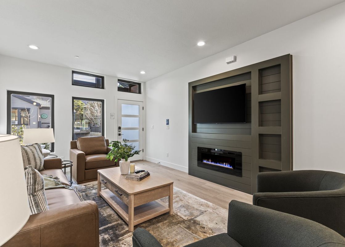 A living room with a fireplace, a large TV, a brown leather sofa, two armchairs, a coffee table and a white lamp.