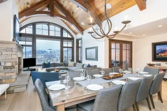 A dining room with a large window overlooking a mountain range, a fireplace, and a chandelier. The dining table is set with plates, glasses, and silverware.
