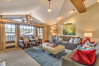 A spacious and inviting living area features comfortable seating, a plush rug, and large windows that offer views of the surrounding area.