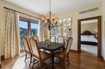 A formal dining area at St Regis Madison Residence with a dark wood table and upholstered chairs, under a grand chandelier, offering a scenic view of mountains through a large window.
