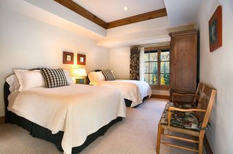 A cozy bedroom in Chateau Beaver Creek Residence 406 with two beds, a large window, and a wooden armoire.