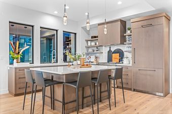 A modern kitchen with white countertops, black stools, and wooden cabinets