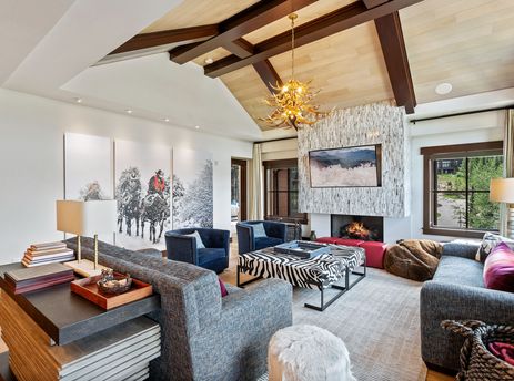 A spacious and elegantly decorated living room with a vaulted ceiling, a stone fireplace, comfortable seating, and large windows offering a view of the outdoors.