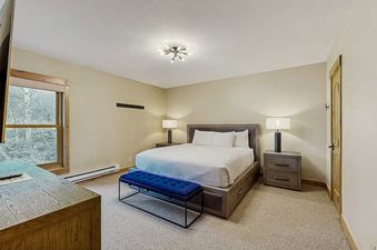A modern master bedroom in Kutuk 211 with a king-size bed, blue velvet bench, and a large window looking out at the trees.